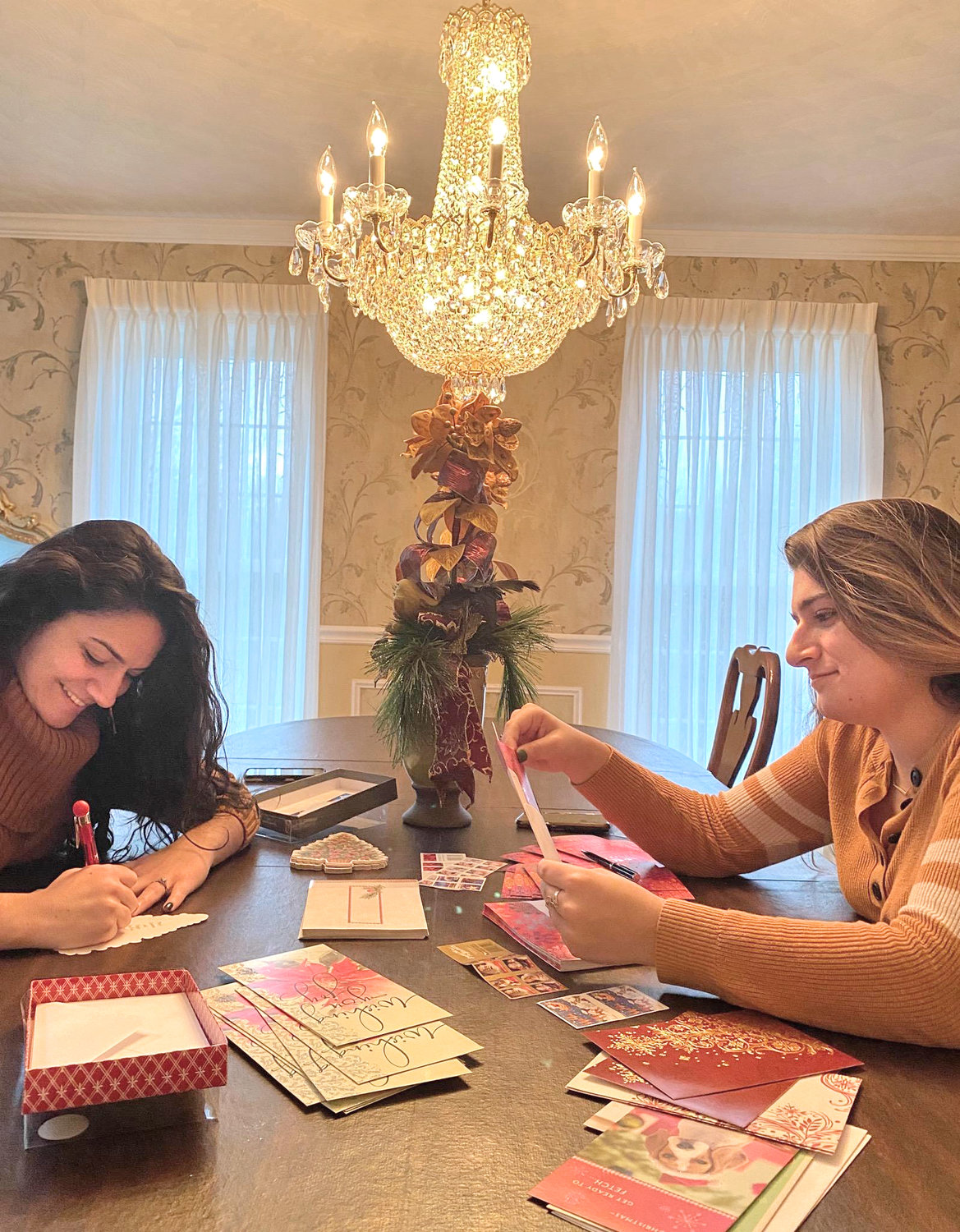 THINKING OF YOU — Alissa and Arica Tehan, of New Hartford, help out by writing messages of holiday cheer as part of the Cards Across America program. Alissa, an insurance professional, and Arica, a pharmacy student, are the granddaughters of Virginia Viscosi, one of the program organizers.