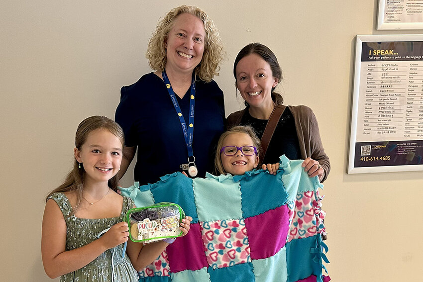 Anna (left) and Grace Chisholm, along with their mother, Rebecca Wilsman (right), delivered toiletry kits and blankets to The Johns Hopkins Hospital&rsquo;s Neonatal Intensive Care Unit, where Grace spent four months after she was born. Grace&rsquo;s primary nurse, Christy Richter (center), coordinated delivery of the gifts.
