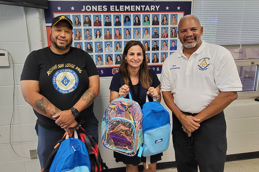 Brother Junior Deacon Bryan Etheridge (left) and Brother Senior Warden Clifford Hopkins (right) delivered backpacks filled with school supplies to Jones Elementary School Counselor Heather Webster.